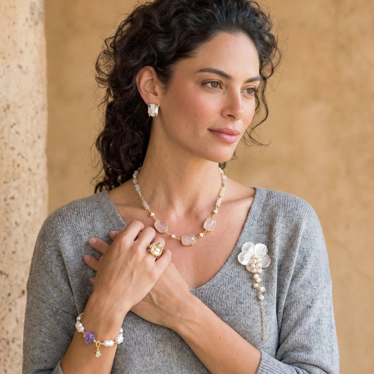 Woman wearing a pink gemstone necklace, pearl earrings, a flower brooch, and a beaded bracelet.